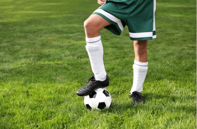 Close up of a boys legs wearing cleets and ball