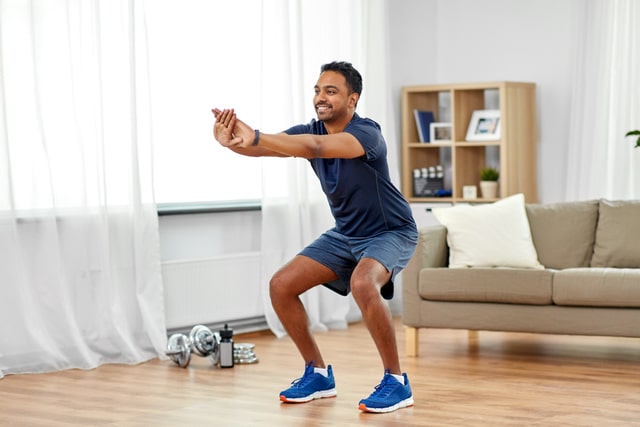 smiling indian man with fitness tracker exercising and doing squats at home