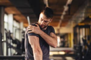 Handsome young man feeling the pain in shoulder at the gym