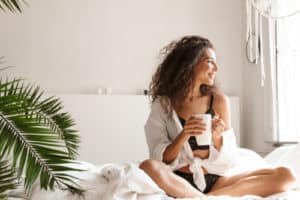 woman wearing lingerie smiling and drinking tea on bed