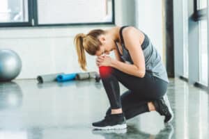 side view of young woman in sportswear having ache in knee while training in gym
